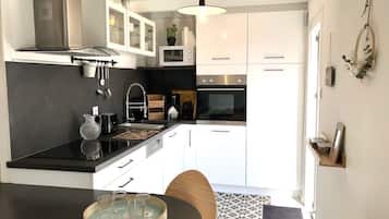 Een moderne keuken met witte kastjes, een zwart aanrecht en een houten eettafel.