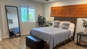 Un dormitorio con cama, una banca, un espejo, una ventana y armarios de madera.