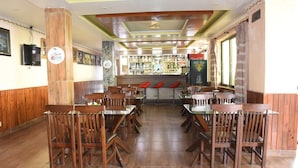 Un restaurante con suelo de madera, varias mesas y sillas, una zona de bar con botellas y un reloj en la pared.