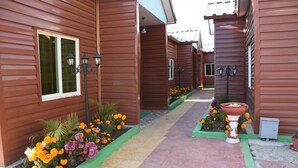 Un pasillo con edificios de madera, macizos de flores e iluminación exterior.