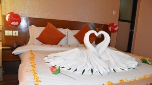 Habitación de hotel con una cama bien hecha, una toalla dispuesta en forma de corazón y una sola rosa sobre la cama.