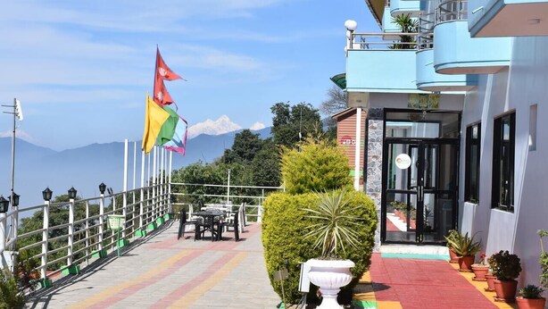 Un hotel con balcón que da a una cadena montañosa, una bandera y plantas en macetas.