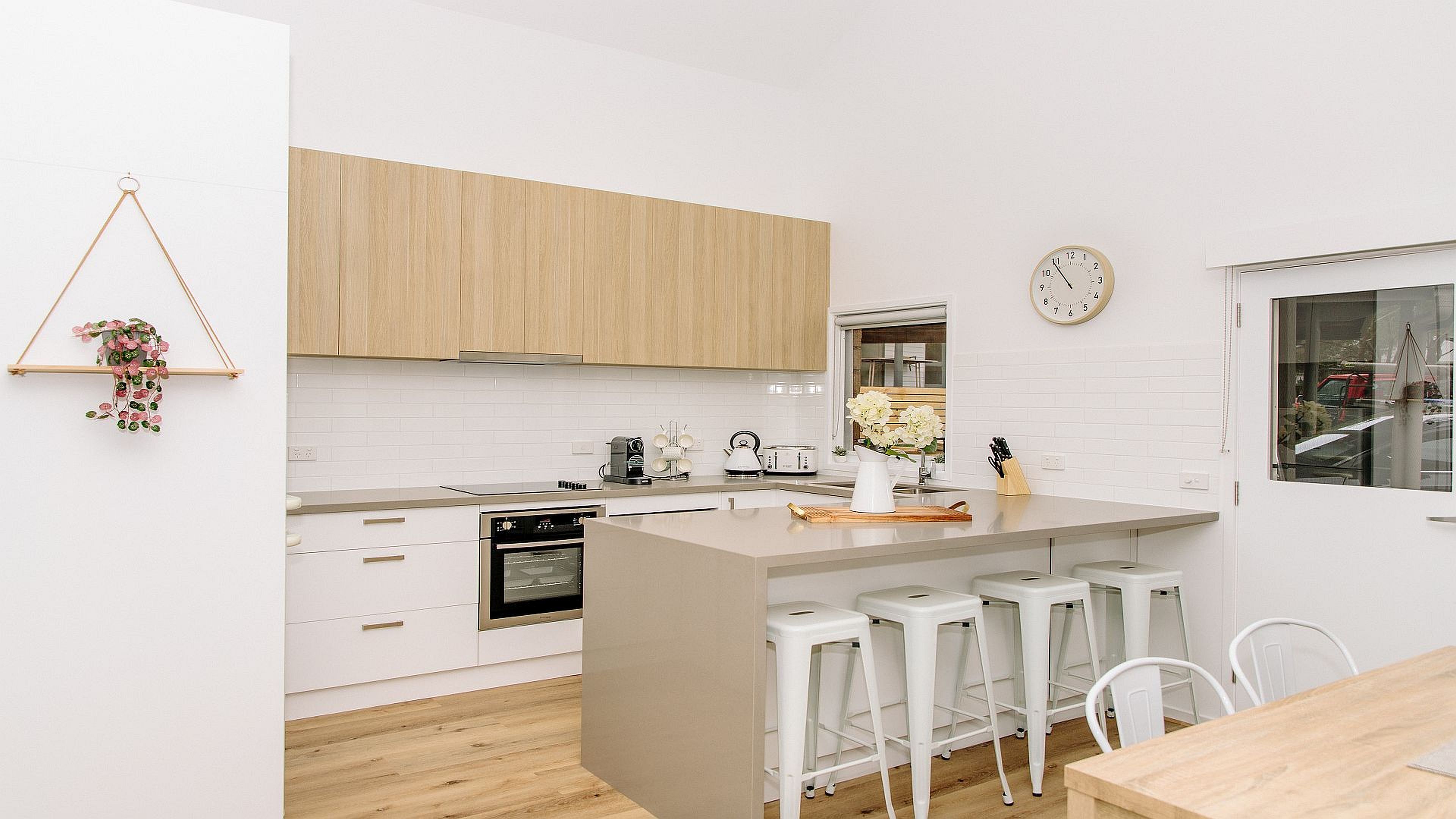 A modern kitchen with white cabinetry, a central island with bar stools, a built-in oven, and a hanging plant.