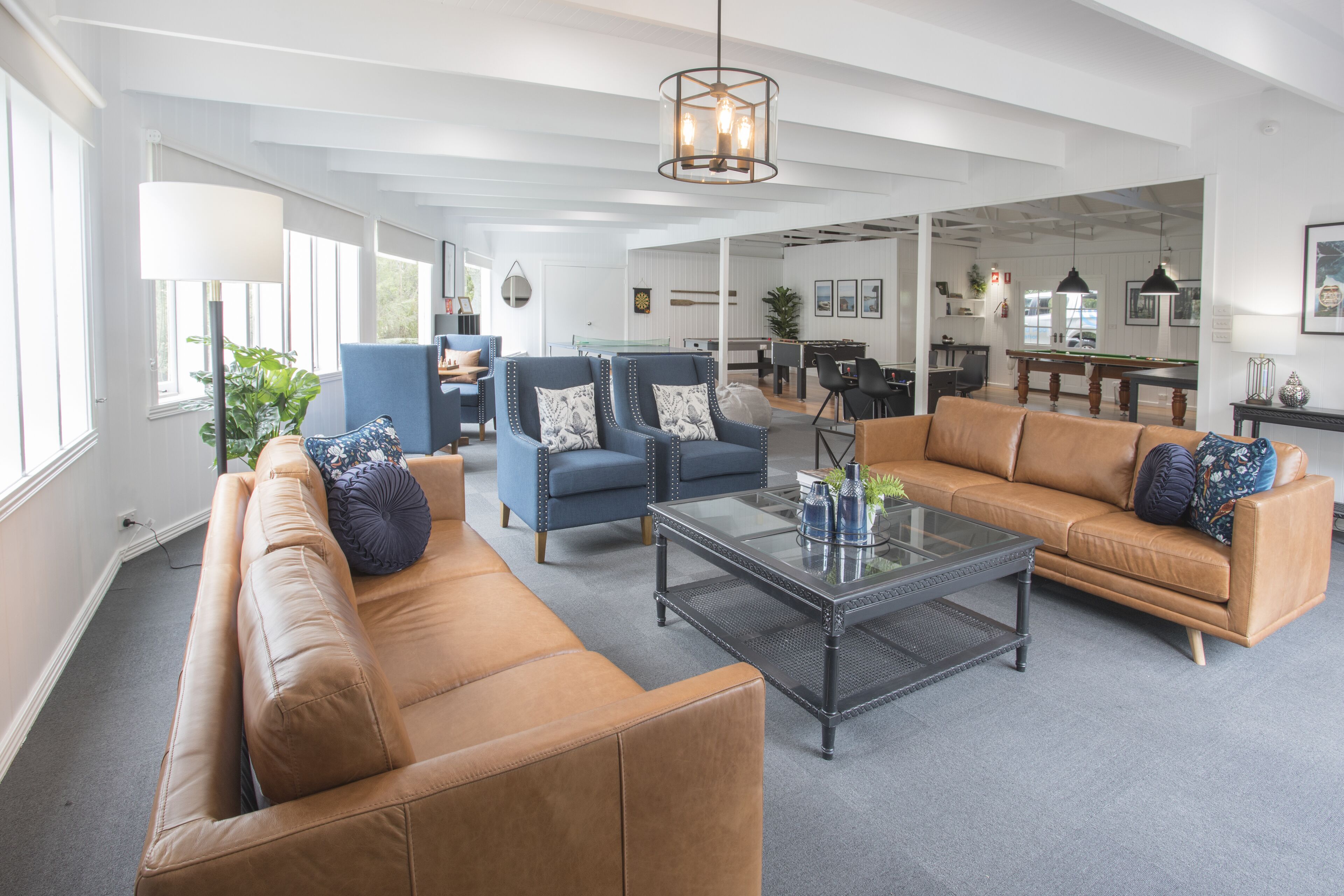 Un salón amplio con un sofá de cuero marrón, sillones azules y una mesa de centro de vidrio.