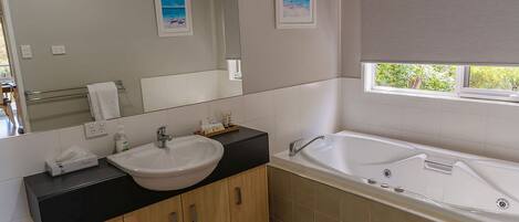 A modern bathroom with a large mirror, a sink, a bathtub, and a window with a view of greenery.