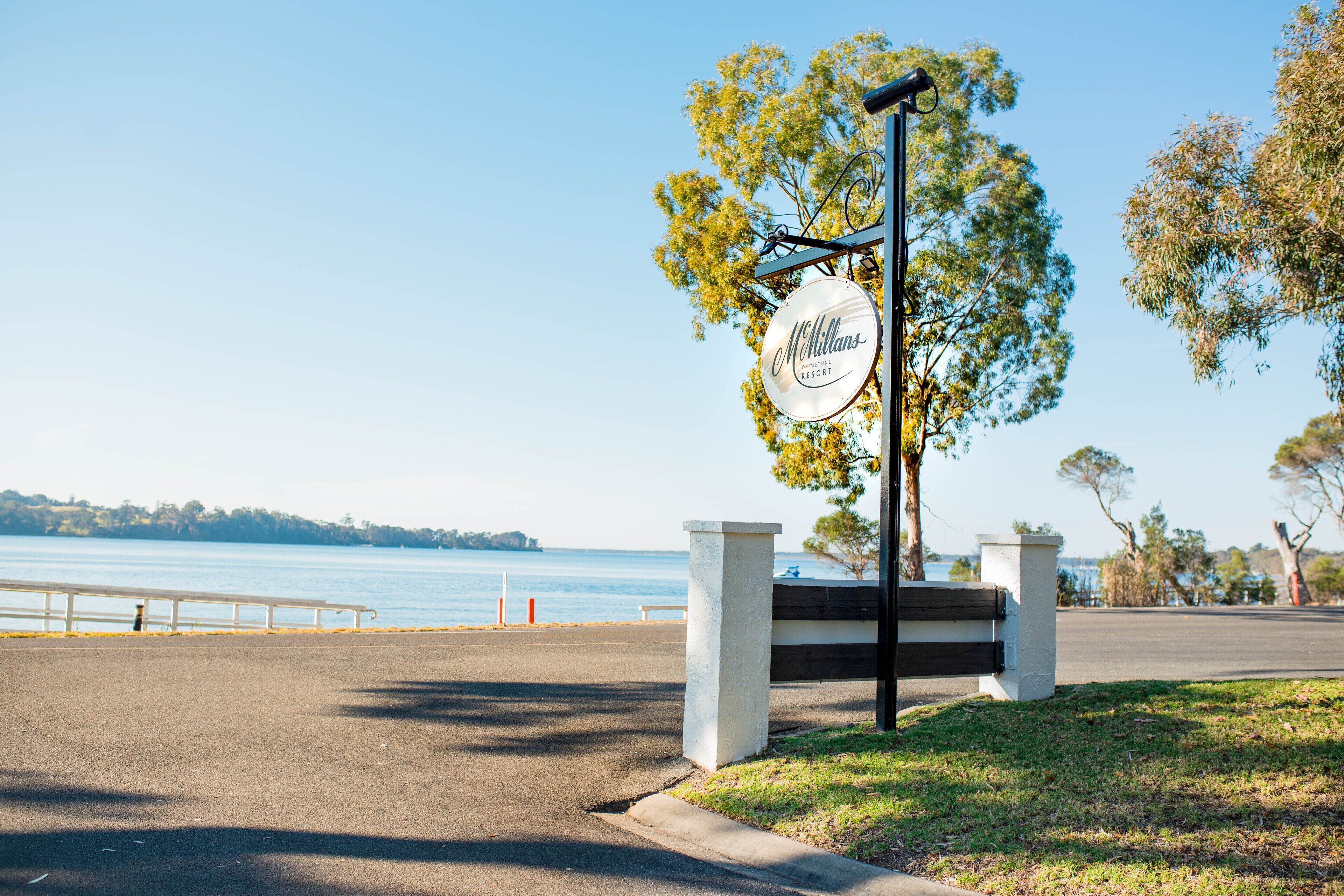 A McMillans Resort sign with a view of the water and a paved pathway leading to the entrance.