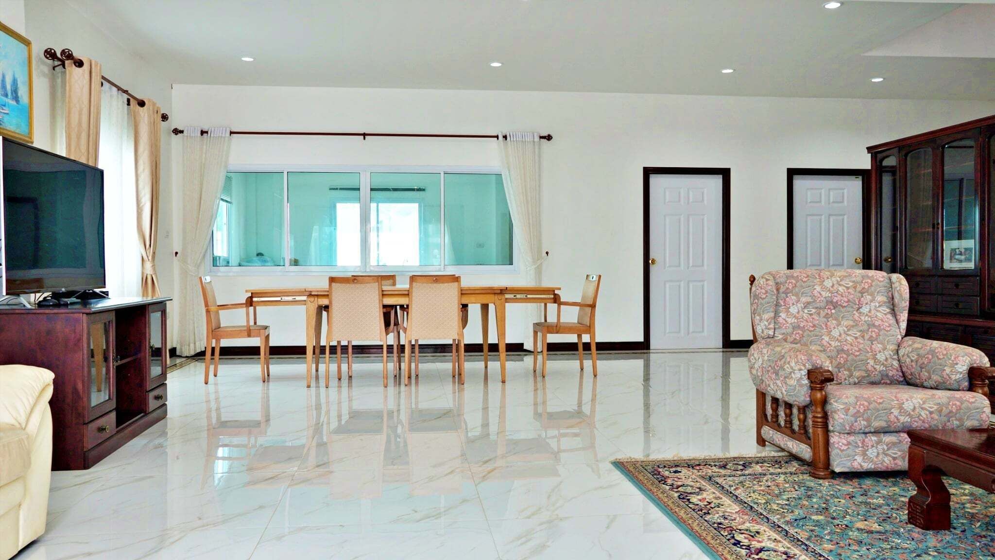 Un salón espacioso con un gran ventanal, una mesa de comedor con sillas, un sofá y un televisor sobre un mueble.