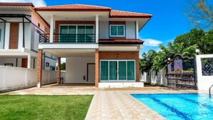 Uma casa de dois andares com piscina, varanda coberta e entrada com portão.