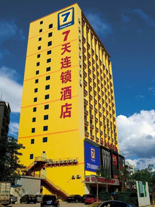 A tall yellow building with a prominent 7Days Inn logo and Chinese characters indicating it is a hotel.