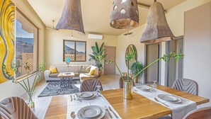 A dining area with a wooden table set for four, surrounded by chairs, with hanging pendant lights above.
