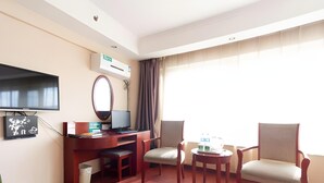 A hotel room with a wooden desk, a flat-screen TV, a mirror, two chairs, a small table with a sewing machine, and a large window with curtains. - Greentree Inn Chaoyang City Chaoyang Street Fangzhi Road Express Hotel (Chaoyang)