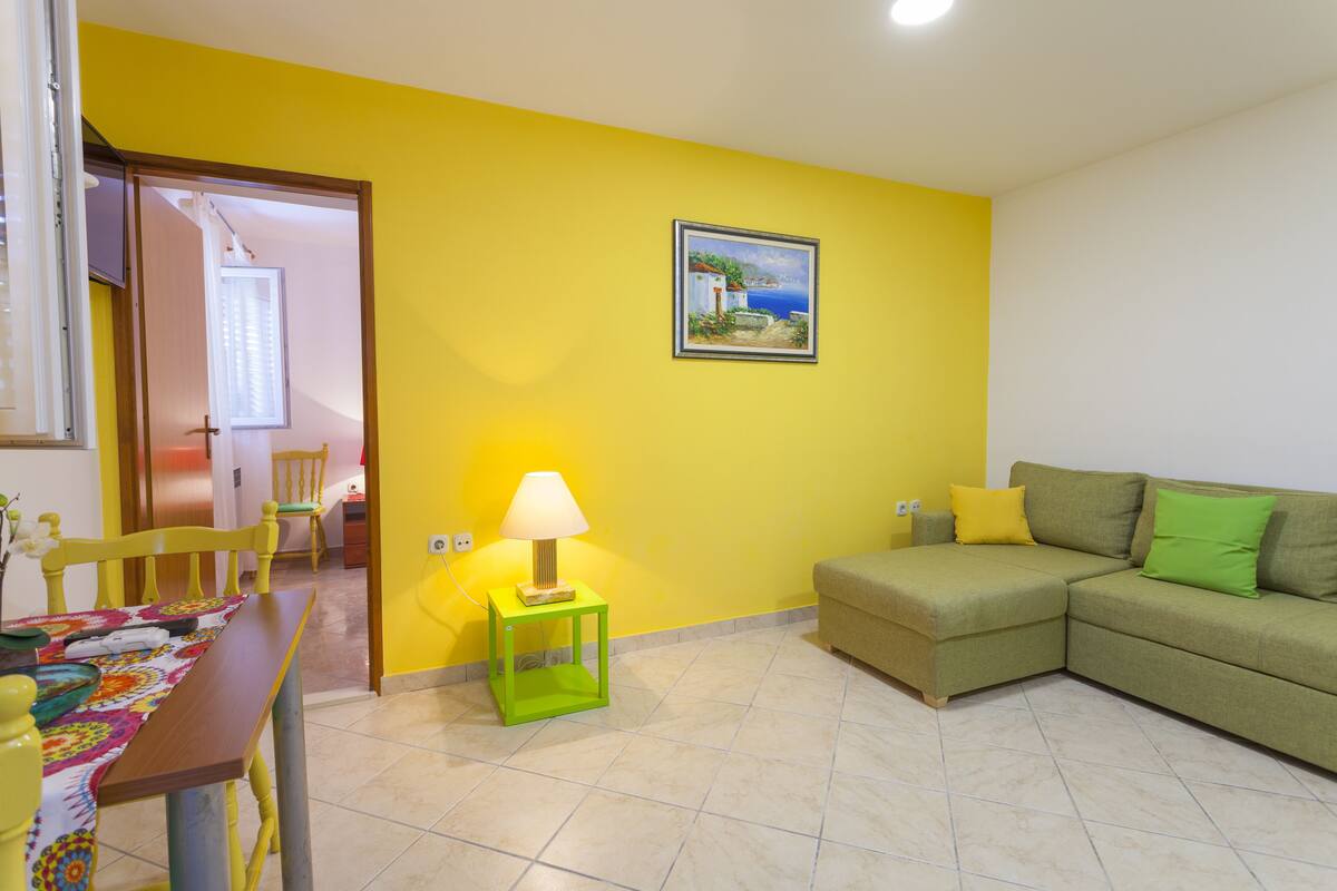 A living room with a green sofa, a dining table with chairs, and a lamp on a green side table.