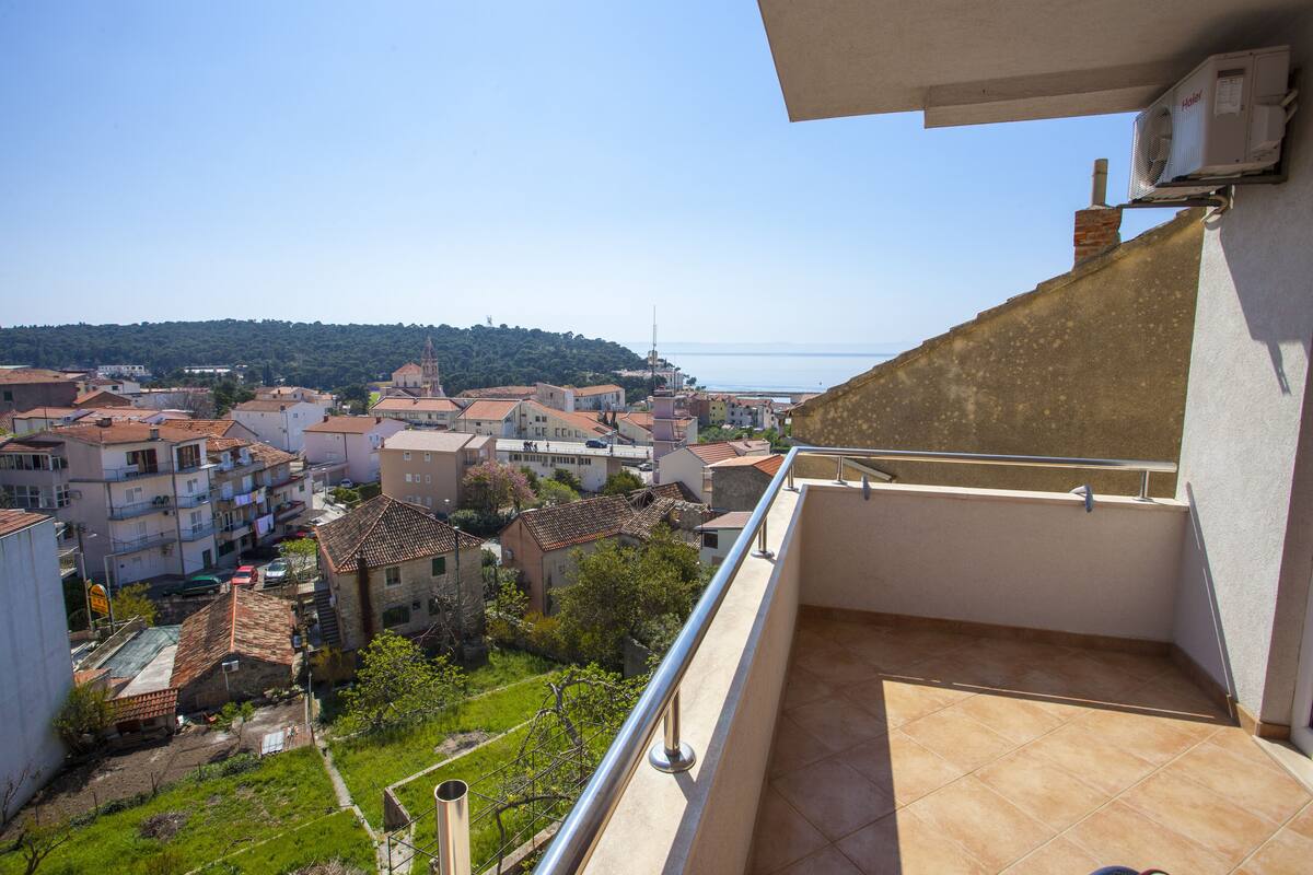A balcony with a view of a coastal town, including buildings and a hill in the distance.