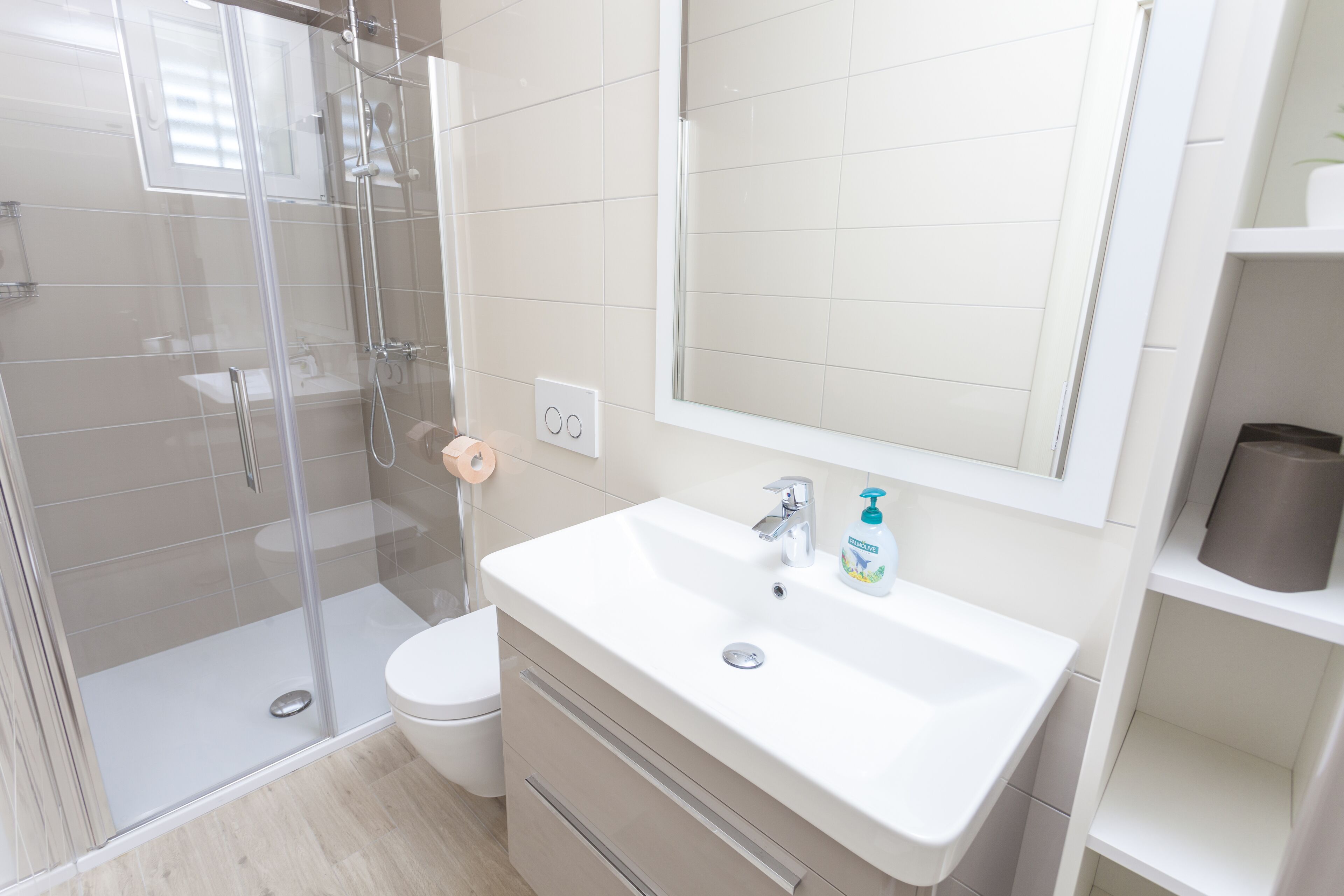A modern bathroom with a glass shower enclosure, a white sink with a mirror above it, and a toilet.