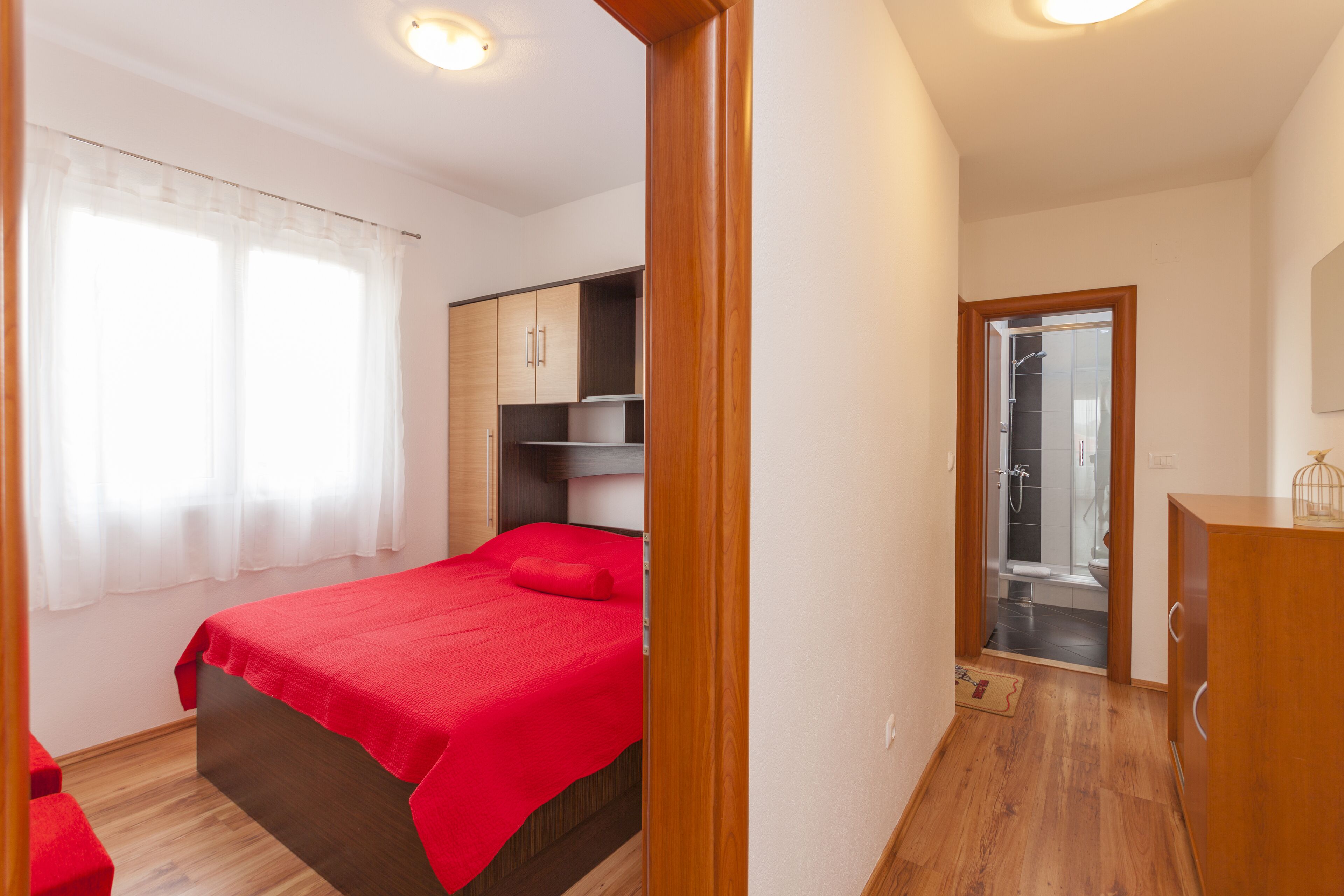 A bedroom with a bed, wooden wardrobe, and a bathroom visible through an open door.