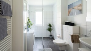 Une salle de bain moderne équipée d’une douche, de toilettes, d’un lavabo et d’une plante en pot.