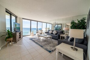 Un salón amplio con un gran ventanal con vistas al océano, un sofá cómodo, una mesa de centro y un televisor sobre un mueble de madera.