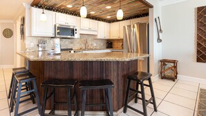 Eine Küche mit Holzbalkendecke, weißen Schränken und einer Arbeitsplatte aus Granit, sowie drei Barhocker.