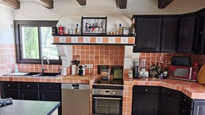 A kitchen with a dishwasher, oven, and a microwave. There is a window providing natural light and a shelf with various kitchen items.