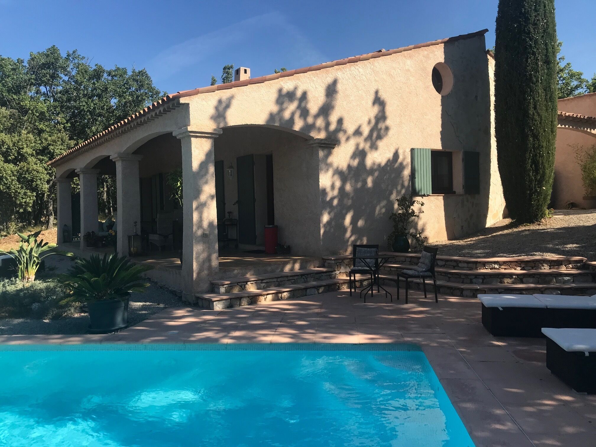 A poolside area with a pool, outdoor seating, and a building with a tiled roof and columns.