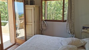A bedroom with a bed, a wardrobe, a window with curtains, and a view of greenery outside.
