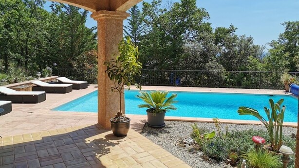 A pool area with lounge chairs, a pergola, and potted plants.