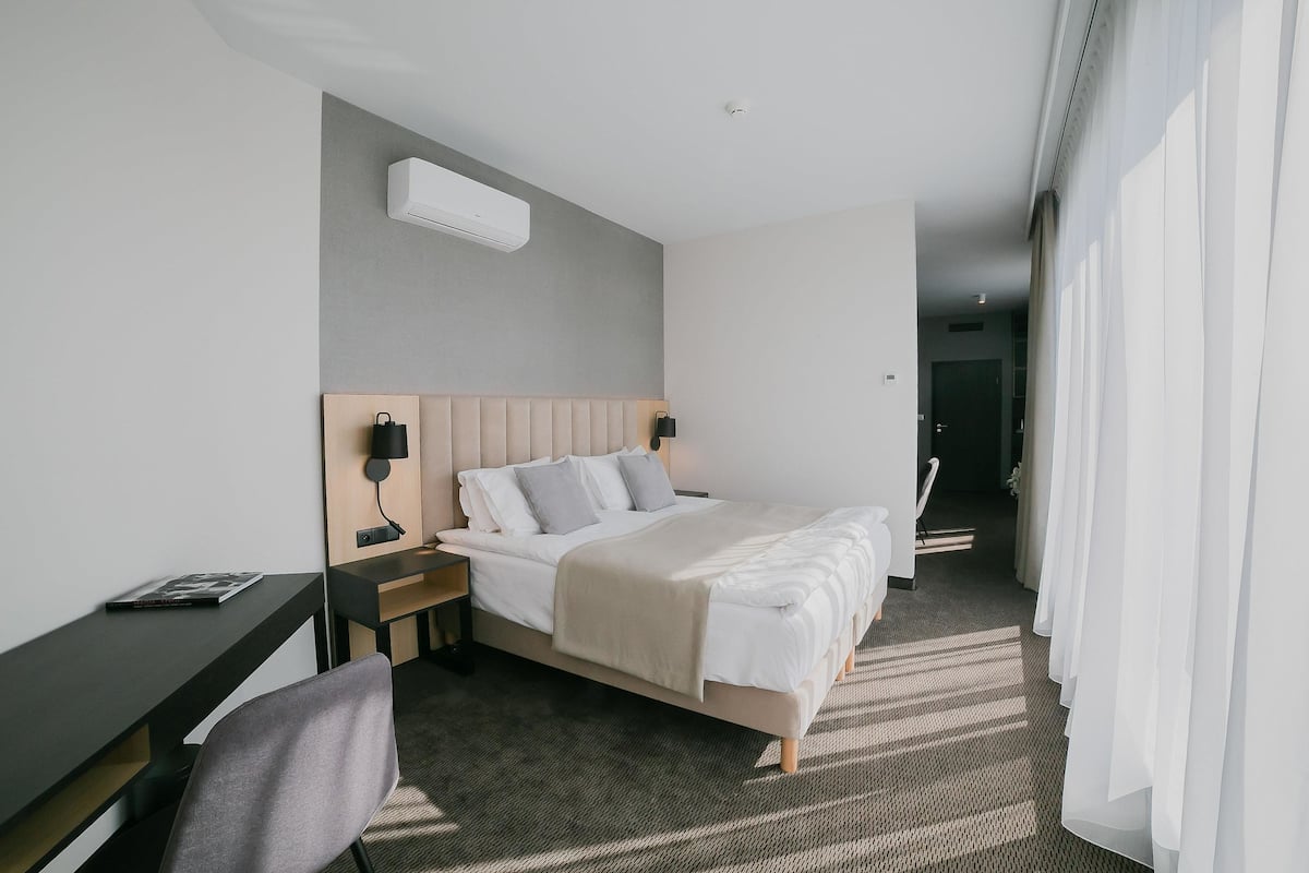 Moderni hotellihuone, jossa on sänky, yöpöydät, työpöytä ja tuoli.
