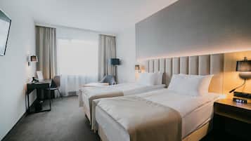Habitación de hotel con dos camas, un escritorio, una silla, una lámpara y un reloj en la mesita de noche.