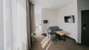 A modern hotel room with a grey sofa, a small table, a TV mounted on the wall, and a door. - B&B HOTEL Warsaw East (Warsaw)