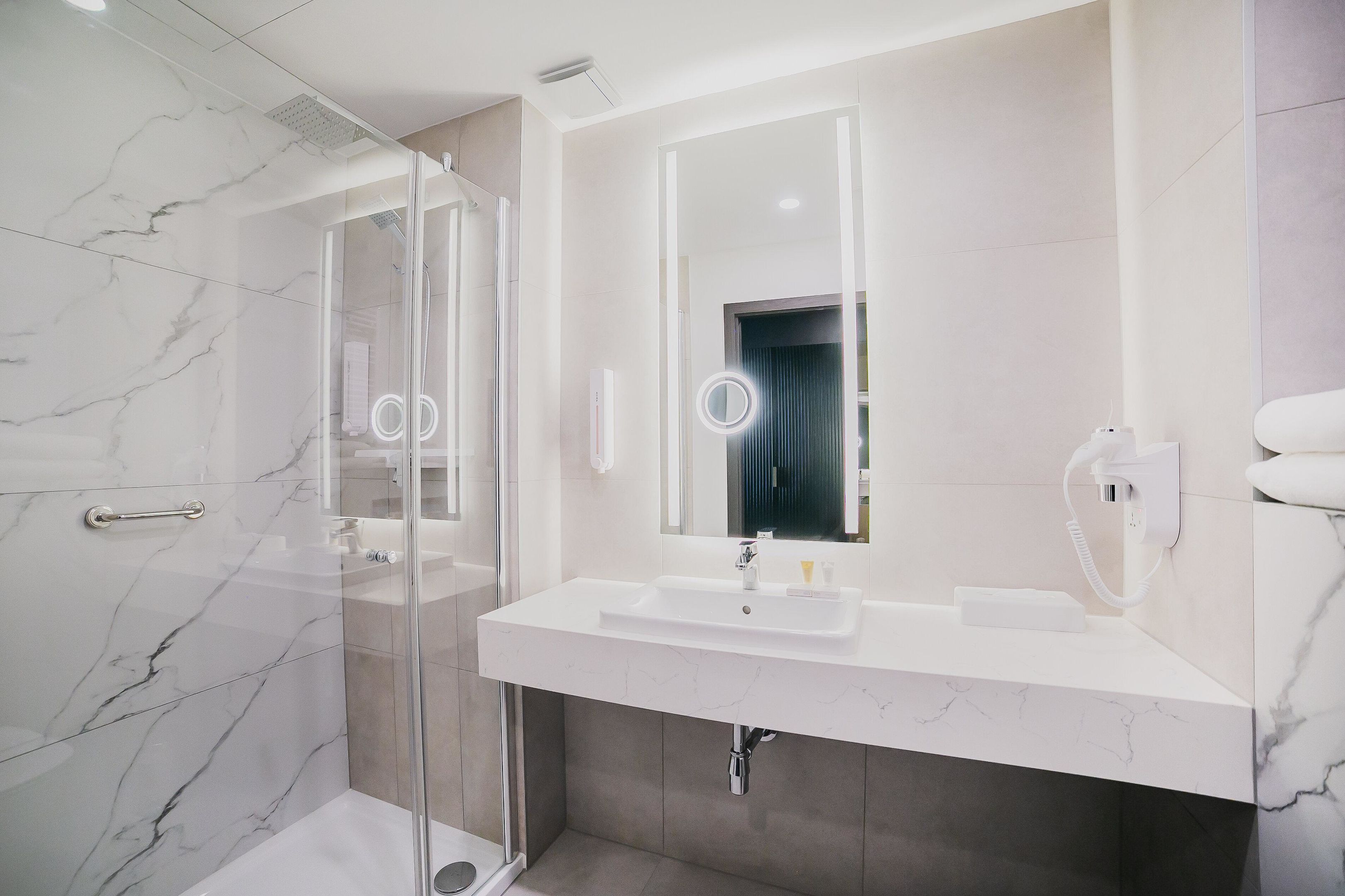 Ein modernes Badezimmer mit Duschkabine aus Glas, einem weißen Waschbecken mit Spiegel und einem Handtuchhalter.