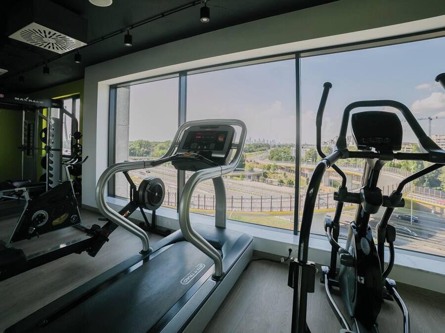A gym with cardio equipment, a weight bench, and a large window offering a view of the city.