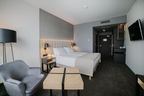 A modern hotel room with a bed, a grey armchair, a small table, a bedside lamp, and a TV mounted on the wall. - B&B HOTEL Warsaw East (Warsaw)