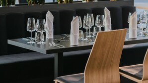 A restaurant with a modern interior, featuring black seating, wooden chairs, and a view of greenery through large windows. - B&B HOTEL Warsaw East (Warsaw)
