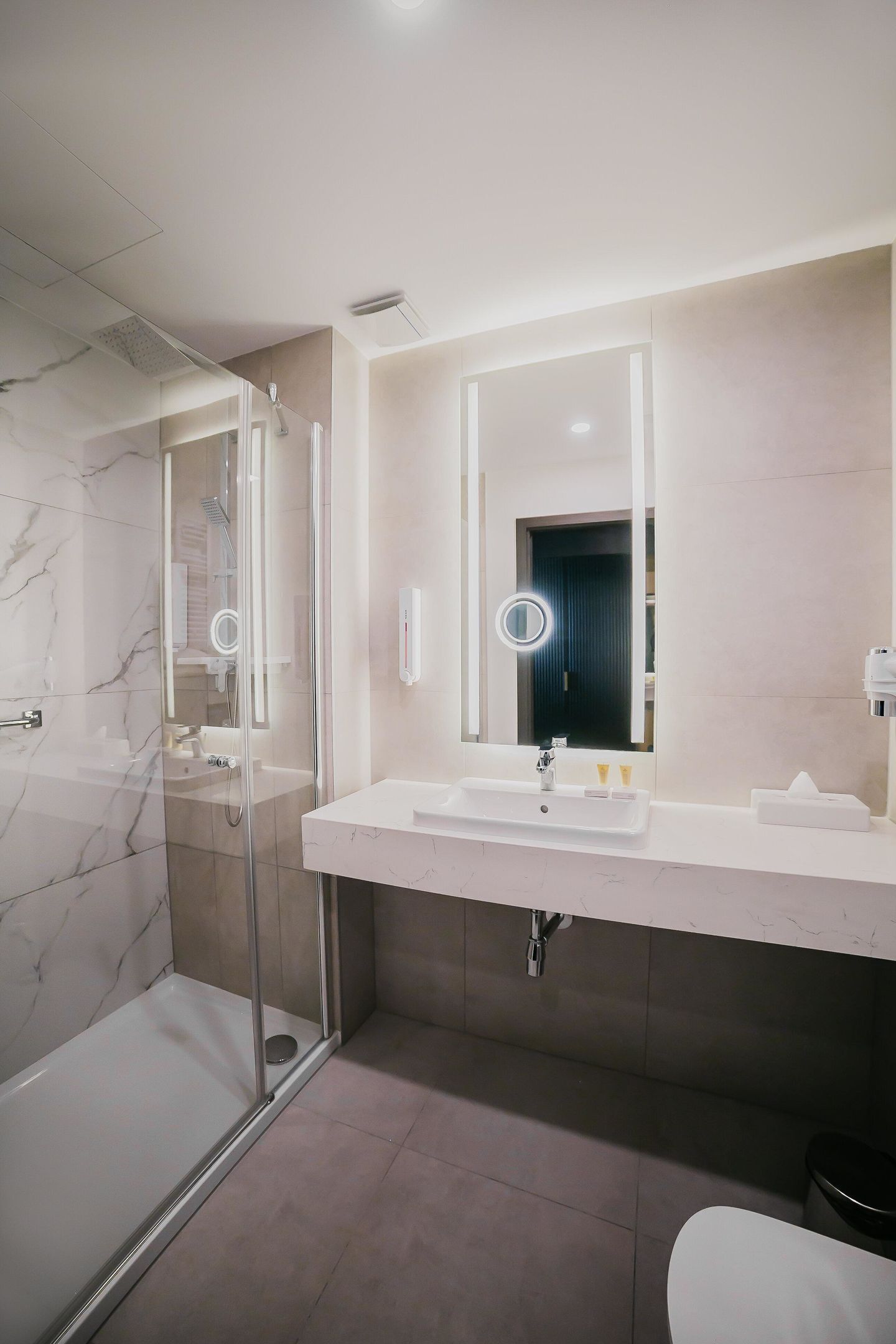A modern bathroom with a glass-enclosed shower, a white sink, and a large mirror with integrated lighting.