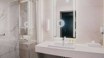 A modern bathroom with a glass-enclosed shower, a white sink, and a large mirror with integrated lighting.