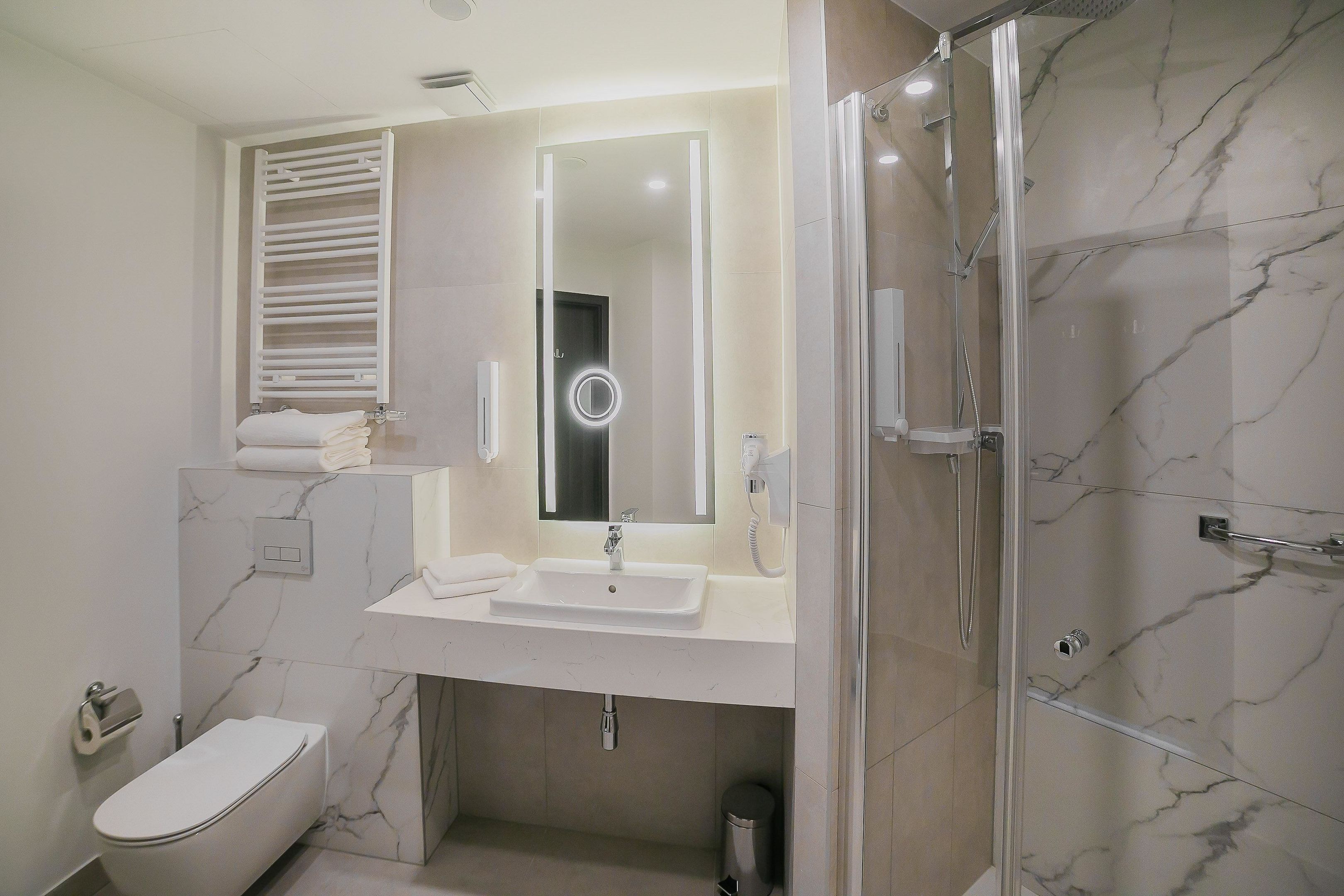 Un baño moderno con un lavamanos, espejo y ducha blancos.