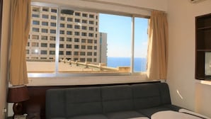 A room with a large window, a sofa, a lamp, and a TV. - Universal Residence (Beirut)