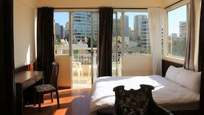 A hotel room with a bed, a desk, and a chair. There is a balcony with a view of the city. - Universal Residence (Beirut)