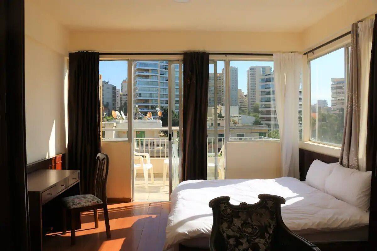 Une chambre d’hôtel avec un lit, un bureau et une chaise. Elle dispose d’un balcon avec vue sur la ville.
