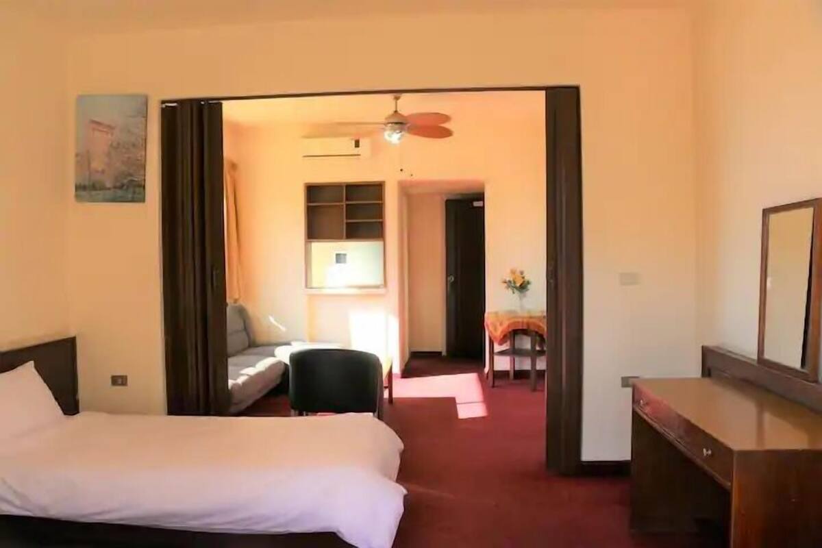 Une chambre d’hôtel avec un lit, un bureau, une chaise et une petite table sur laquelle se trouve un vase.