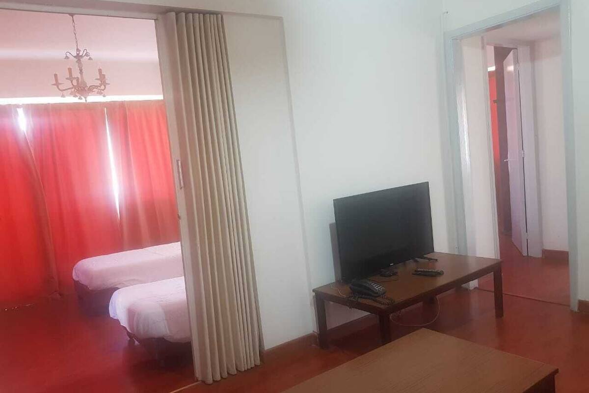 Une chambre avec deux lits, un téléviseur posé sur une table en bois et une moquette rouge.