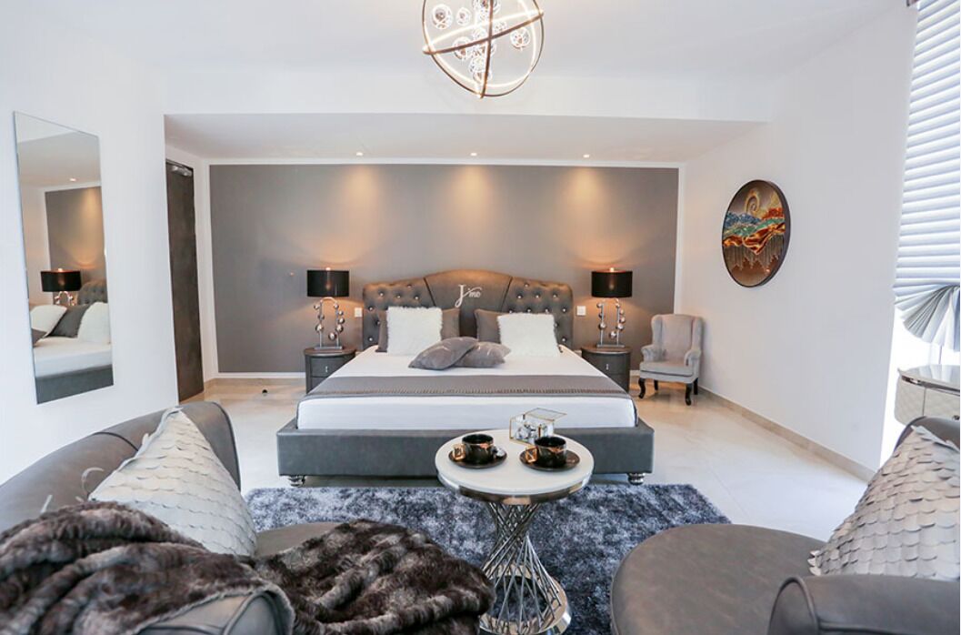 A modern bedroom with a large bed, bedside tables, a chair, and a small table with cups.