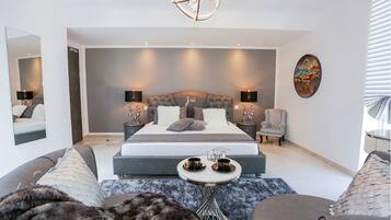 A modern bedroom with a large bed, bedside tables, a chair, and a small table with cups.