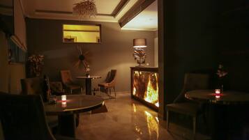 A dimly lit lounge area with a round table, chairs, a sofa, and a decorative lamp.