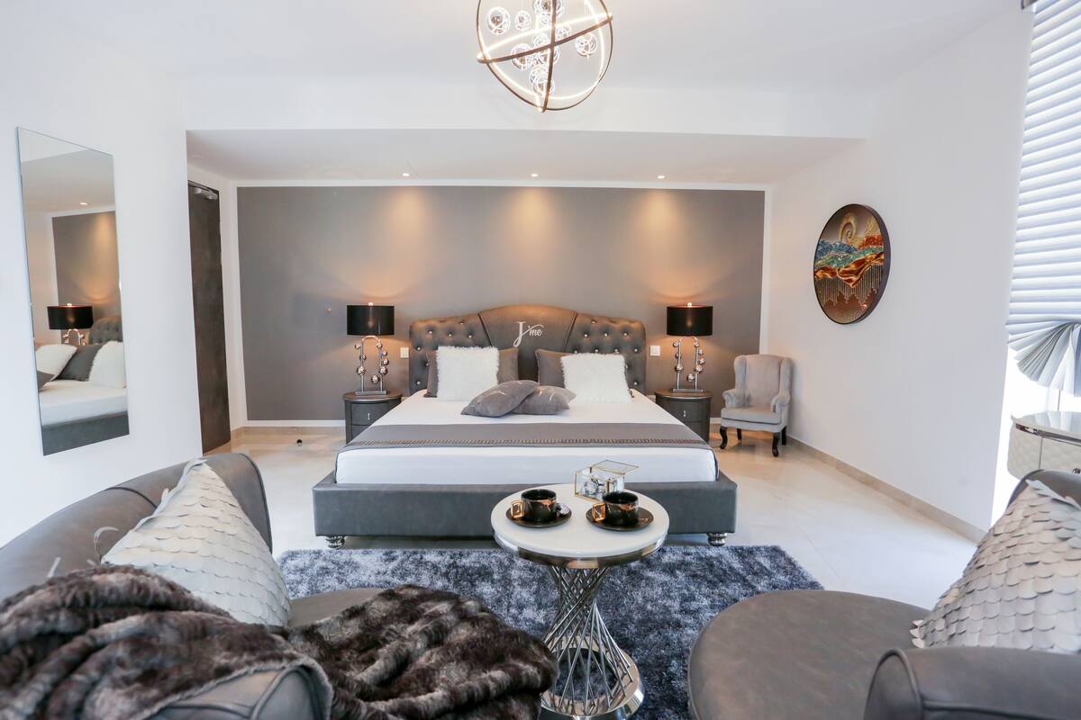 Ein modernes Schlafzimmer mit einem großen Bett, Nachttischlampen, einem kleinen runden Tisch mit Tassen und einem Wanddekor.