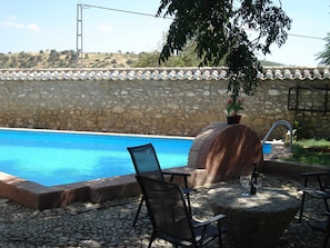 Ein Swimmingpool mit Steinmauer und Flachdach, umgeben von Sitzgelegenheiten im Freien und einem Blumentopf.