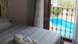 Ein Schlafzimmer mit Bett, Handtüchern und Blick auf ein Schwimmbad und Berge.