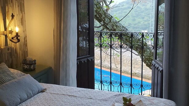 Ein Schlafzimmer mit Bett, Nachttisch, Lampe und Blick auf Pool und Berge.