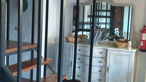 Ein Zimmer mit einer Holztreppe, einem weißen Schminktisch mit Schubladen, einem Spiegel und einem Feuerlöscher an der Wand.