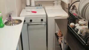 A compact kitchen with a stove, oven, and sink. There is a dish rack with plates and cups, and a small trash bin. - PALAZZINA LA TORRE VIA CRFINUIM 4 (L'Aquila)